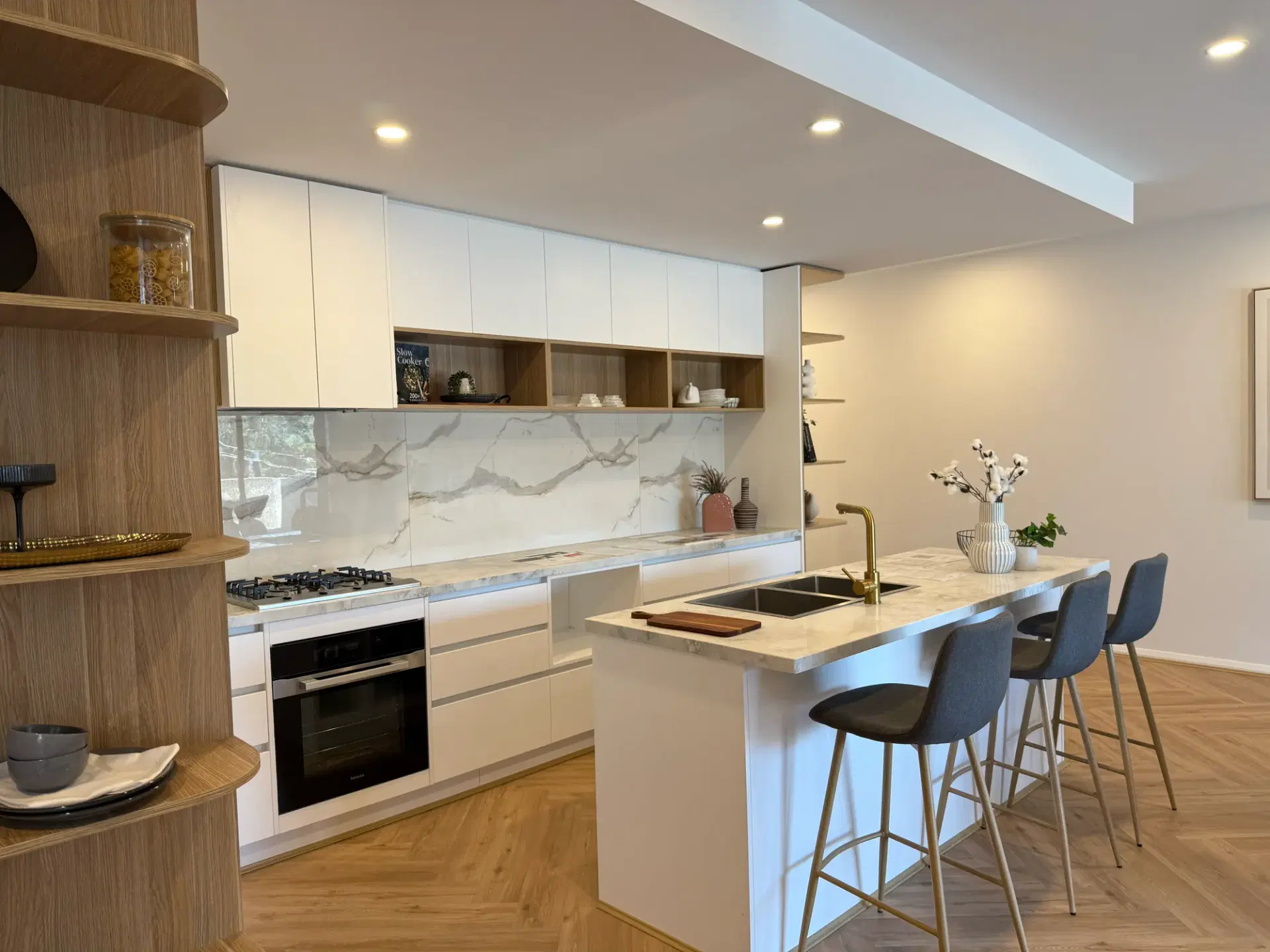 Kitchen in a Heidelberg apartment with a stone island bench, bar stools and curved open shelving