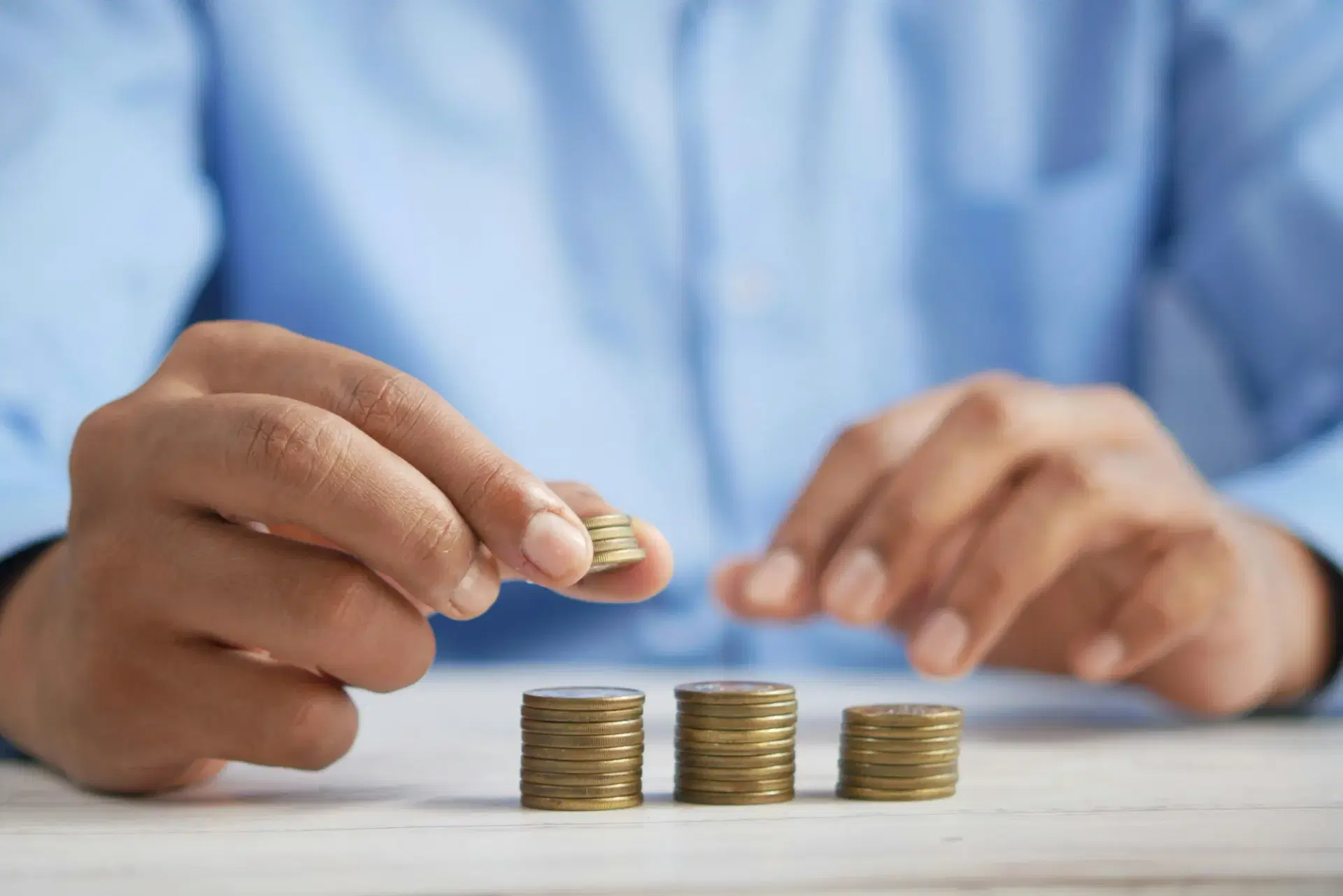 Hands adding a coin to three growing stacks of coins on a desk