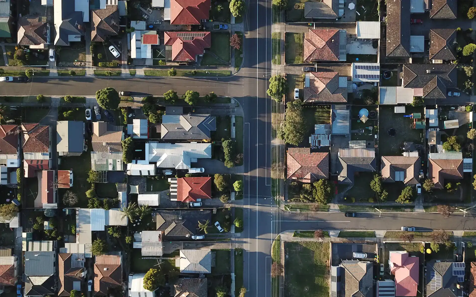An overhead aerial view at golden hour of the kind of established eastern-Melbourne streetscape Wantirna is made up of — tiled rooftops, generous backyards and tree-lined residential streets meeting a main road