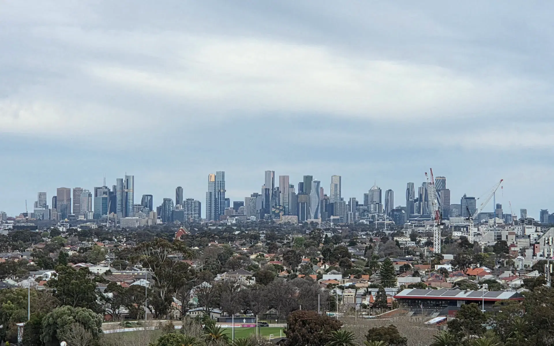 A Melbourne cityscape in which apartment and office towers rise directly behind a dense neighbourhood of low-rise houses, the two kinds of property whose land content differs most